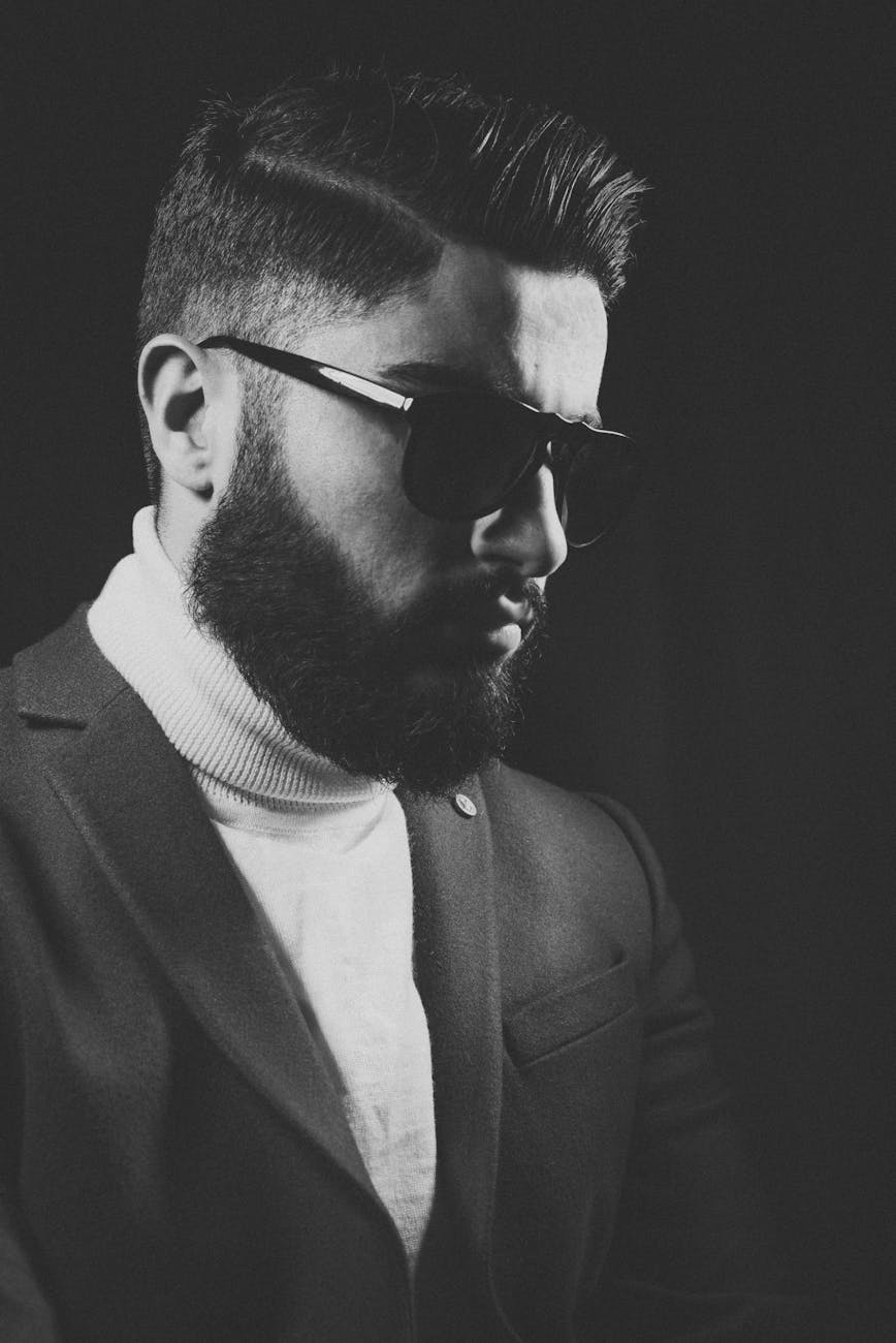 Black and white portrait of a stylish bearded man wearing a suit and sunglasses.